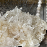 A cluster of clear quartz crystals with sharp, pointed formations, set against a blurred background with bead-like elements.